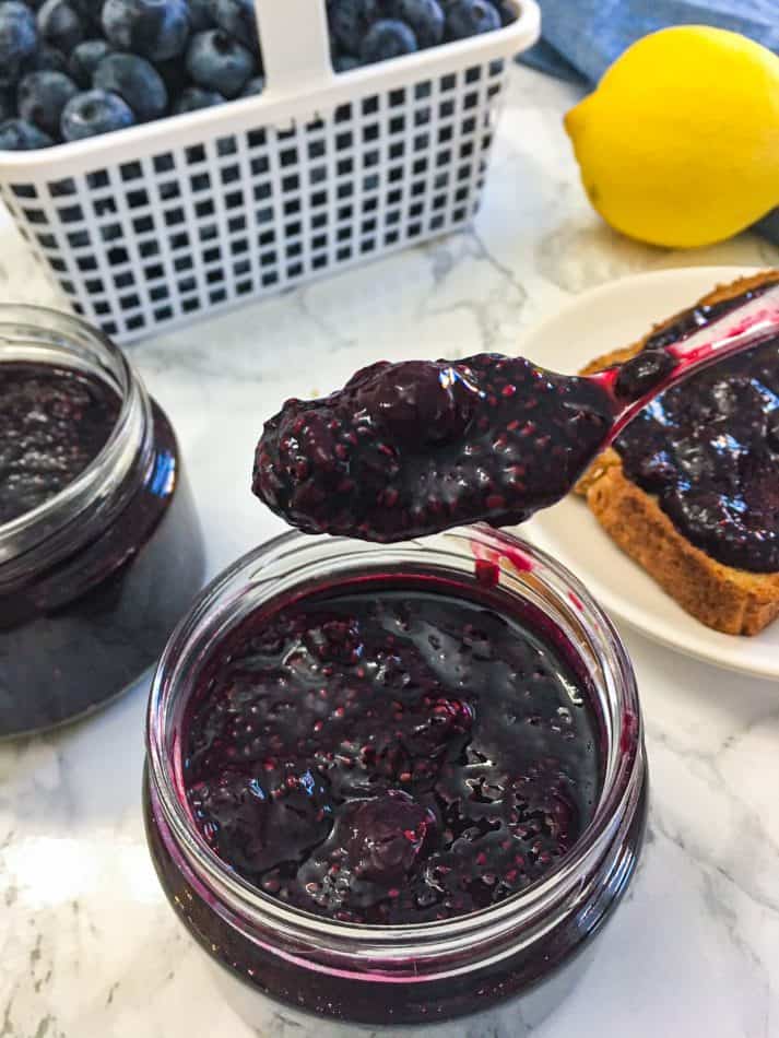 spoon of blueberry jam being held over jar