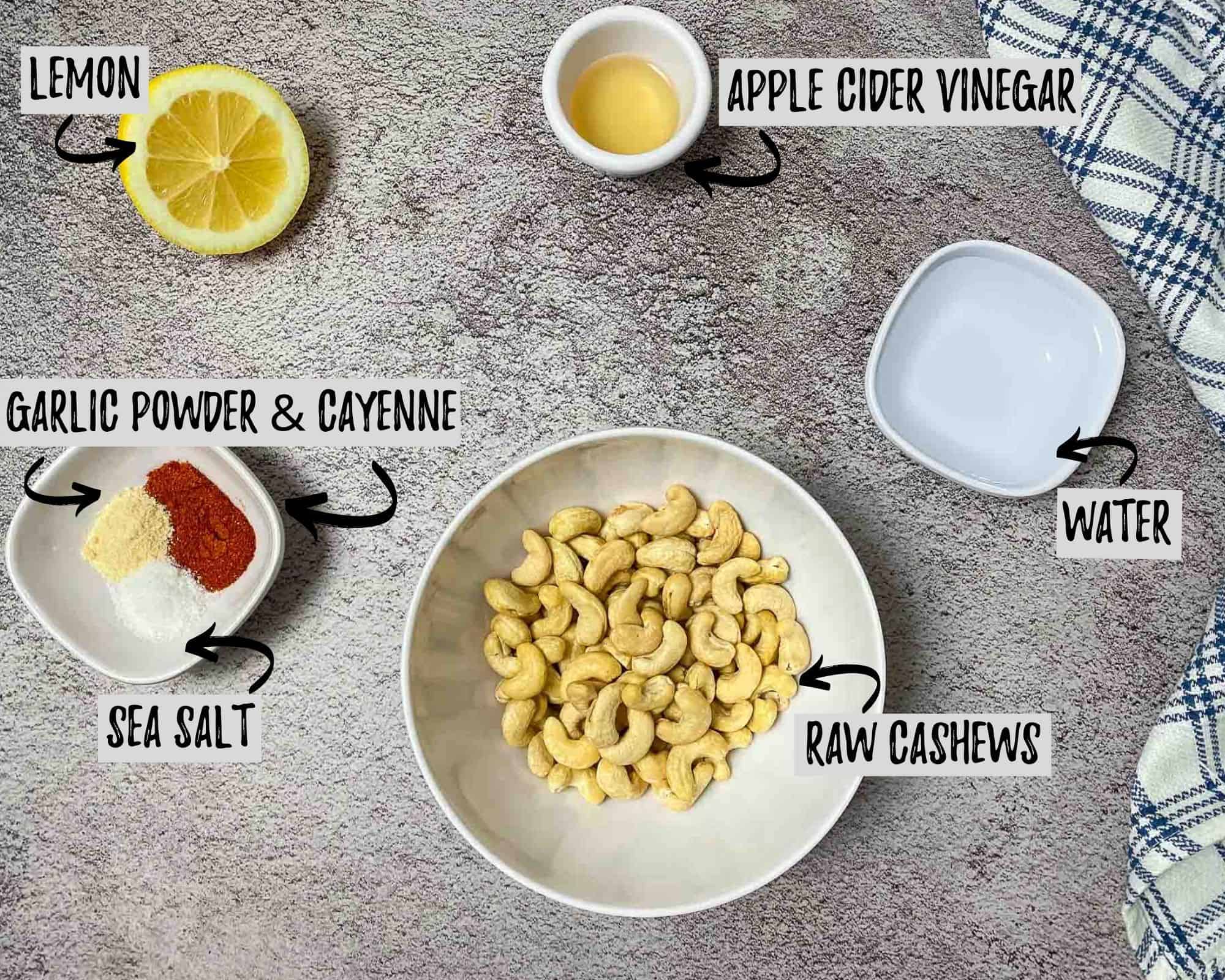 bowl of raw cashews, cup of apple cider vinegar, bowl of water, half a lemon and a bowl of seasoning