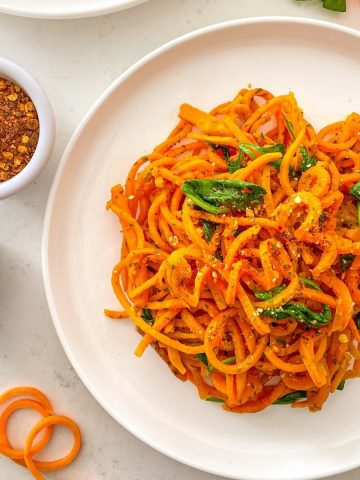 Plate of sweet potato noodles with wilted spinach and chili flakes on top.