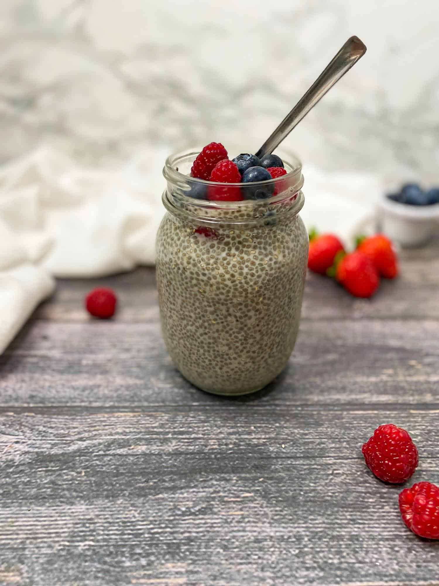 Chia pudding in glass jar with fresh berries on top and spoon inside