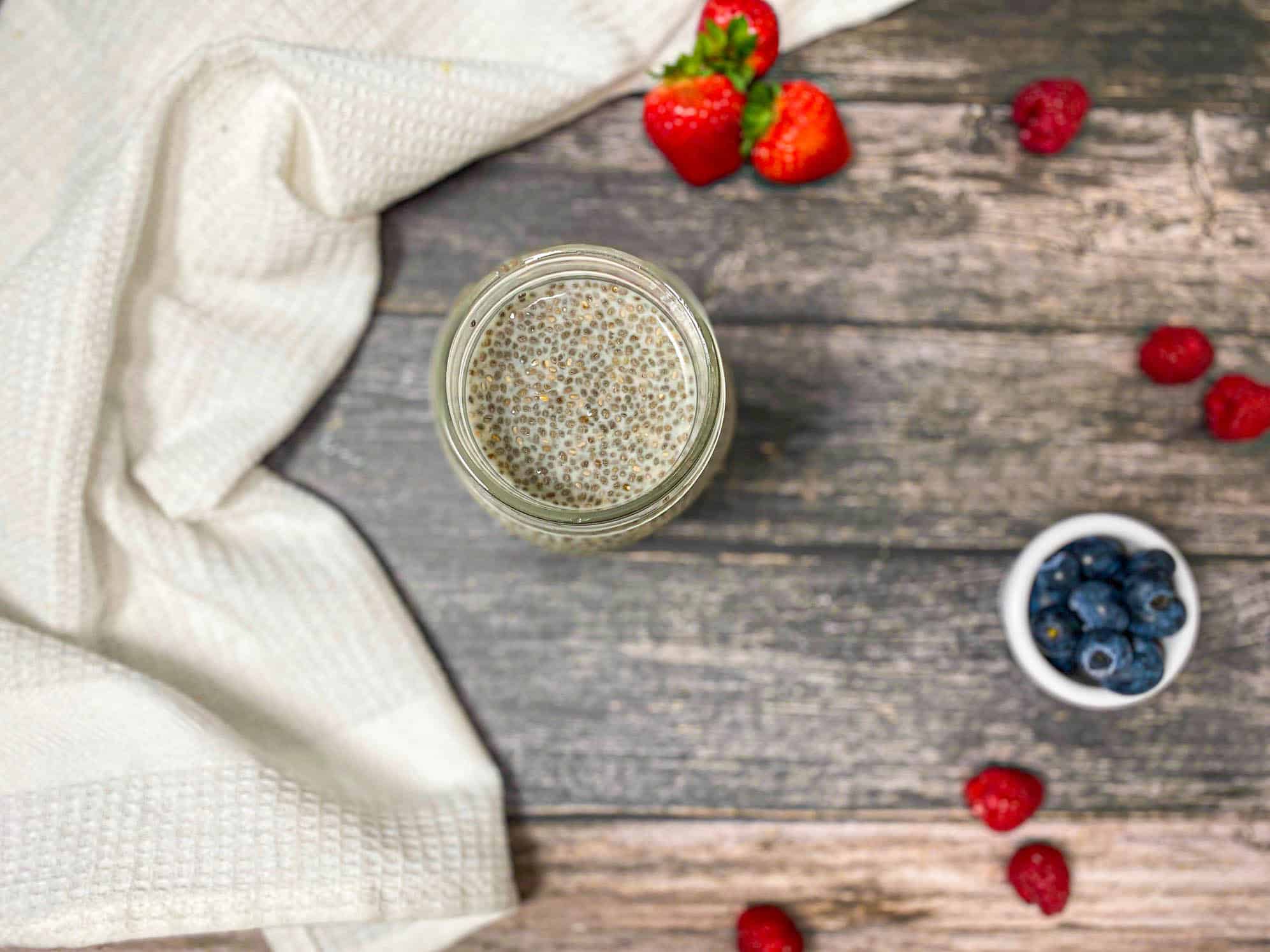 Over head view of glass jar with milk and chia seeds inside and berries around it.