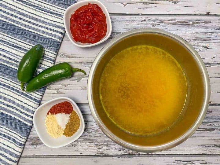 broth in bowl with tomato paste and seasoning in small bowls and jalapenos beside them