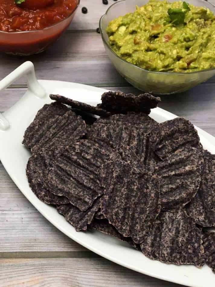 plate of black bean chips with bowl of salsa and bowl of guacamole 