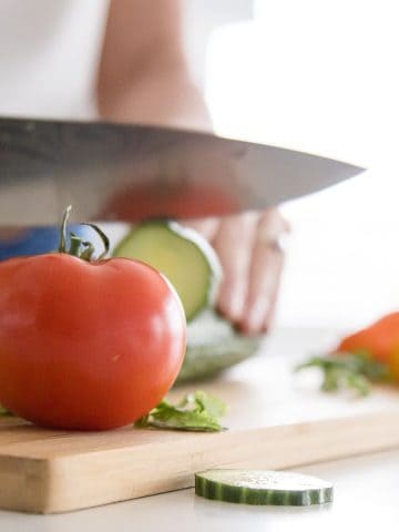 Knife slicing cucumber on cutting board.