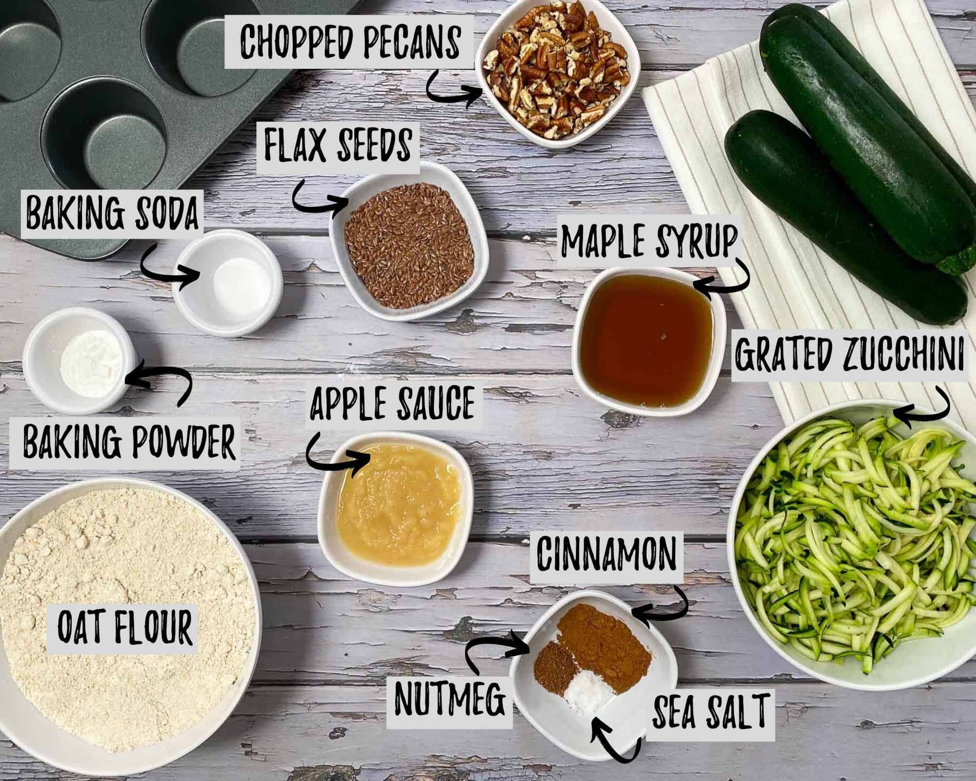 ingredients for muffin prep: bowl of flour, bowl of grated zucchini, seasoning, nuts, maple syrup, apple sauce, flax seeds, baking powder and soda