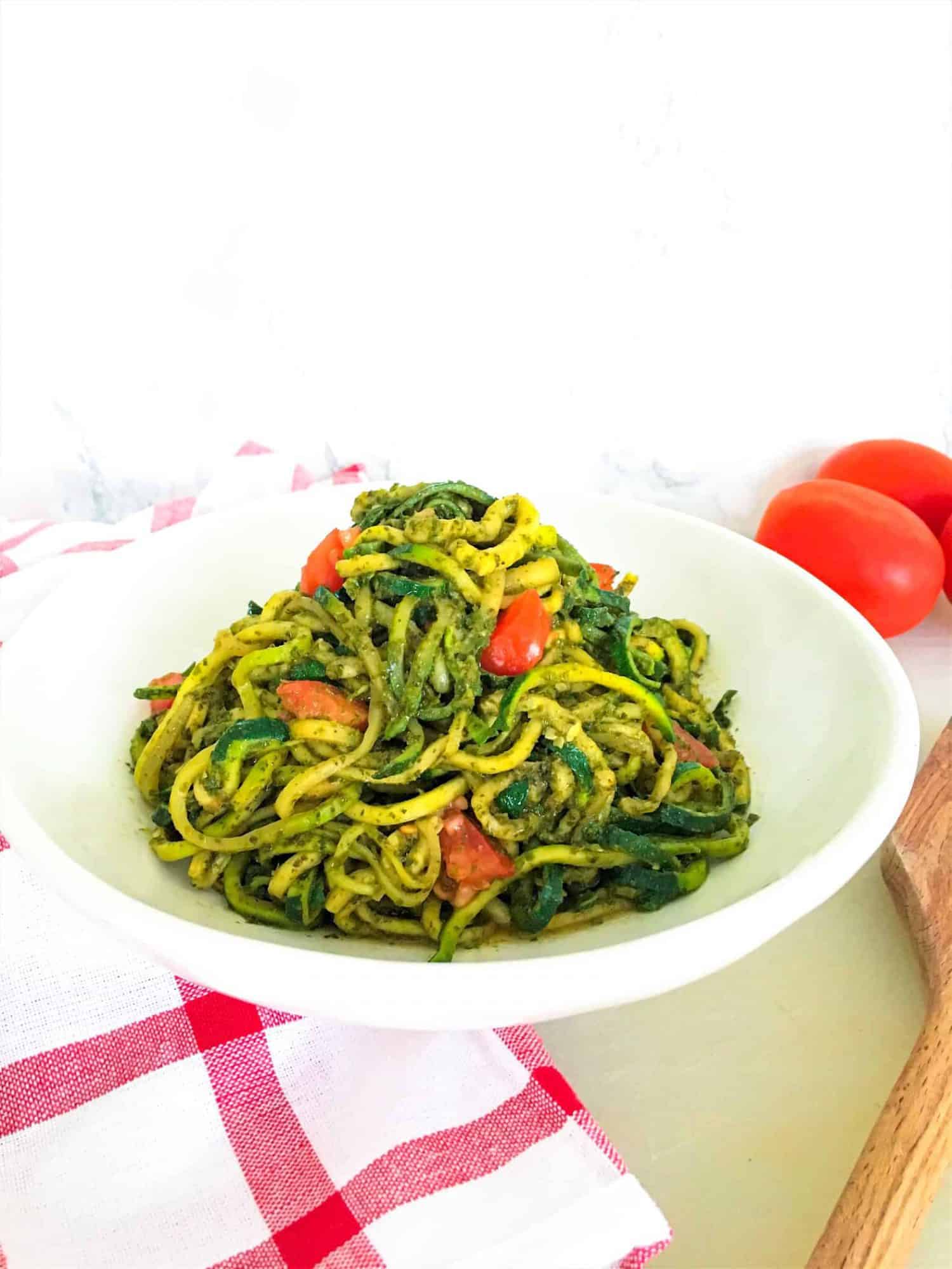 pesto zucchini noodles in plate with tomatoes in background