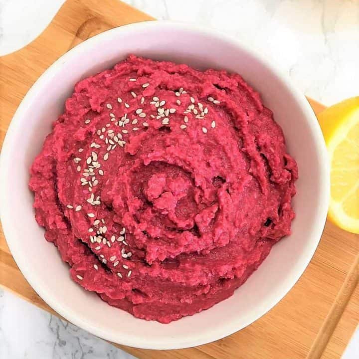 beet hummus in bowl garnished with sesame seeds