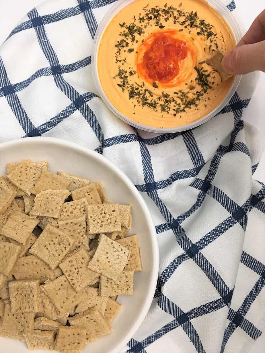 white bean protein crackers being dipped into roasted red pepper hummus