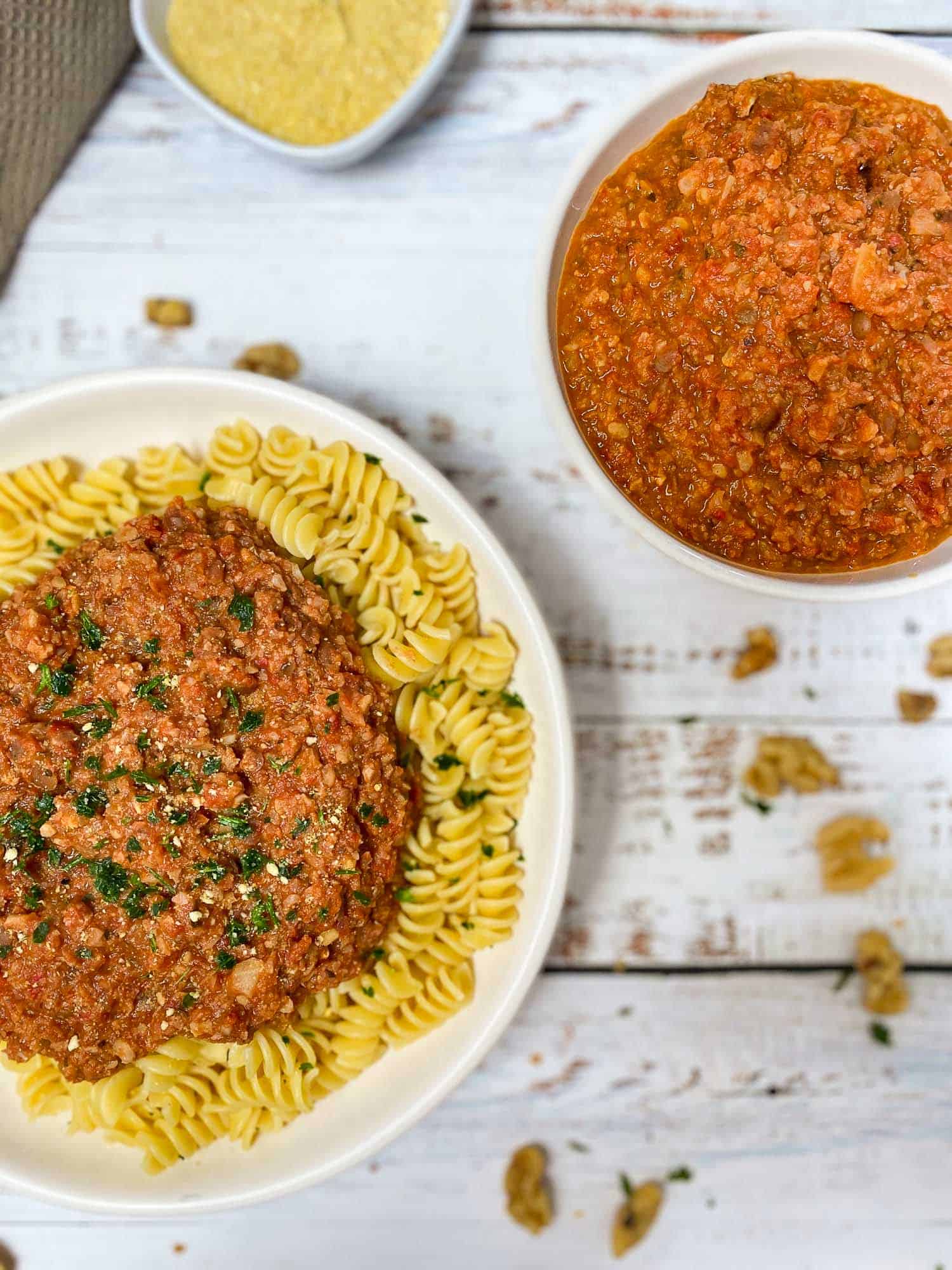 plate of pasta with sauce on top and bowl of bolognese sauce beside it
