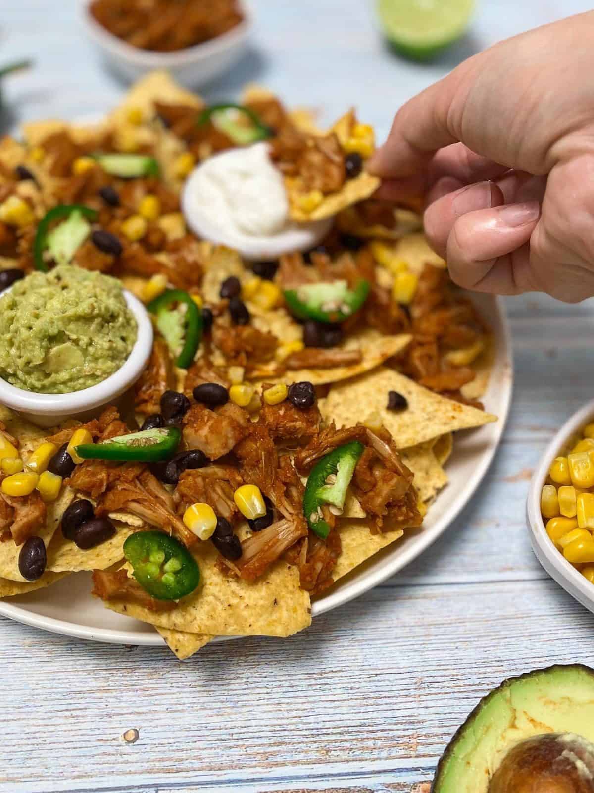 chip being dunked into bowl of sour cream in the center of a platter of nachos