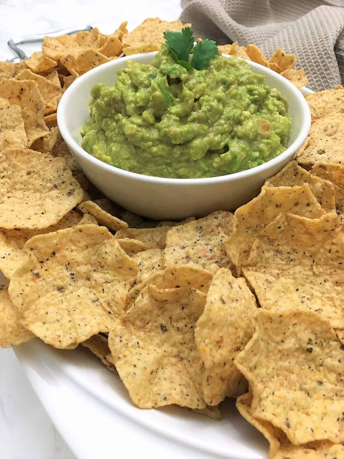 white bowl of guacamole with tortilla chips around the bowl