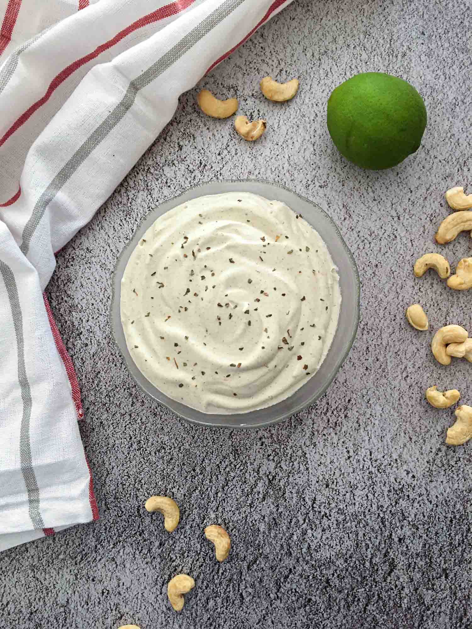 vegan ranch dressing in glass bowl with cashews scattered around it