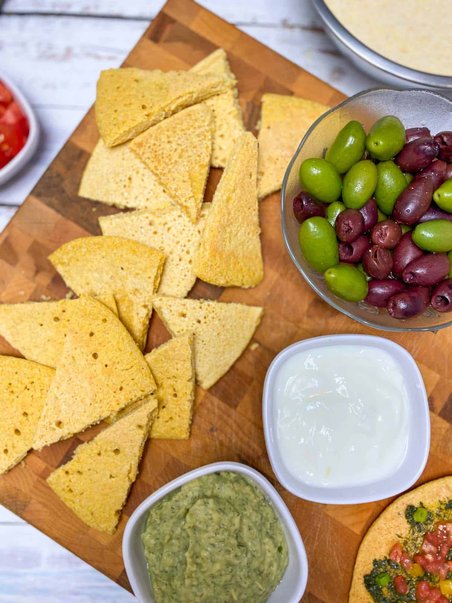 triangular wedges of socca on cutting board with bowl of olives and dips