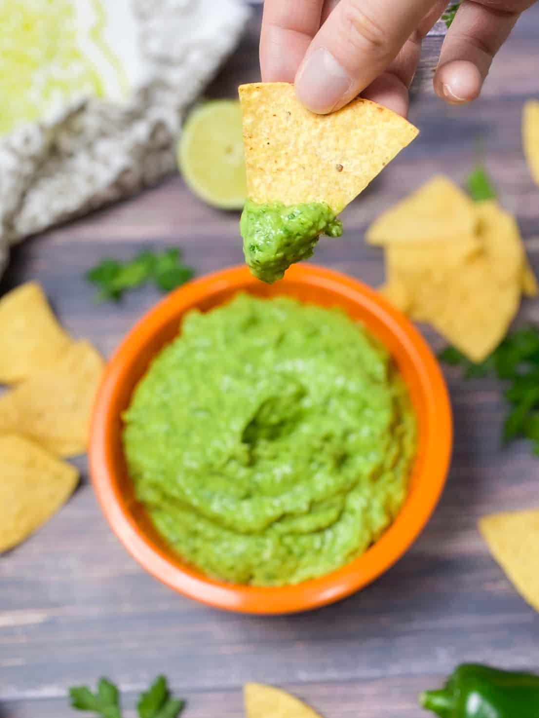 tortilla chip dunked in guasacaca being held up over the bowl of dip