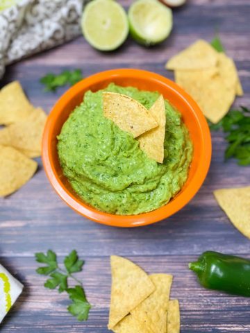 two tortilla chips resting in the center of a bowl of guasacaca dip
