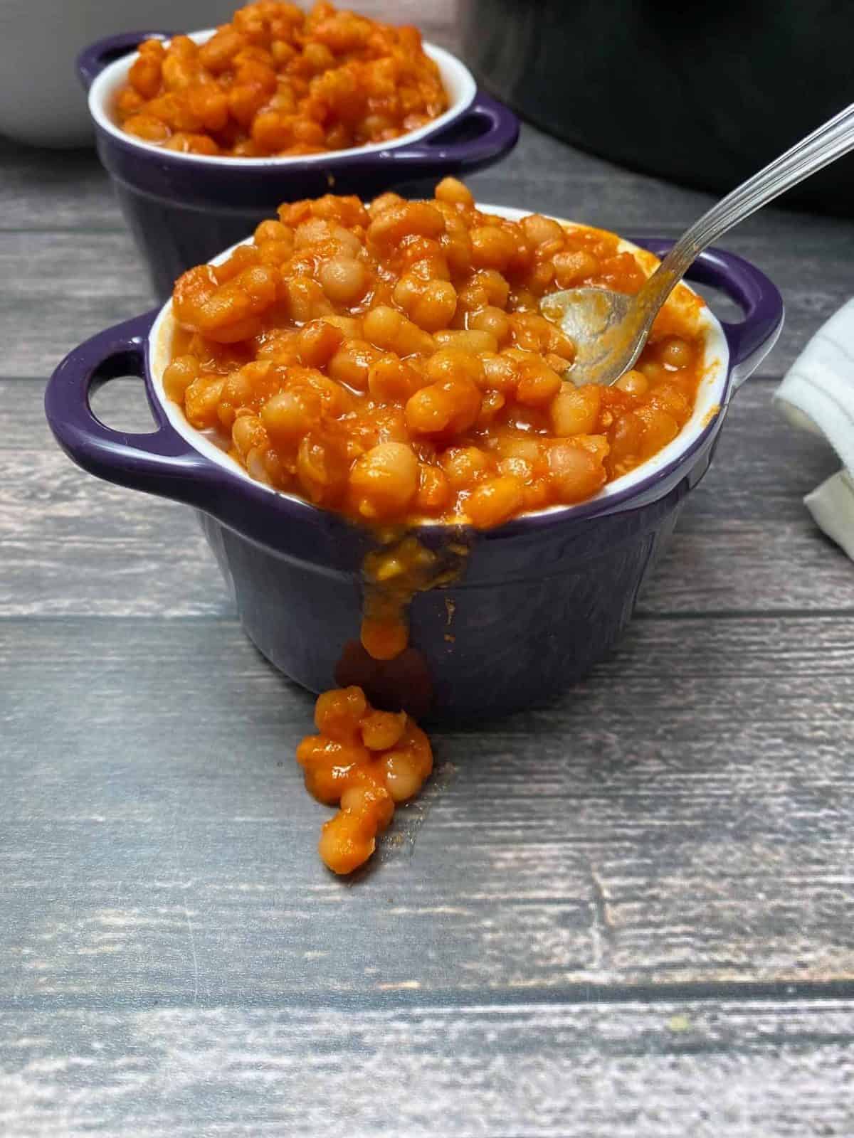 cooked beans in sauce spilling over the side of purple bowl