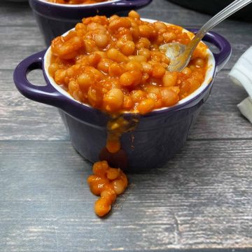 cooked beans in sauce spilling over the side of purple bowl