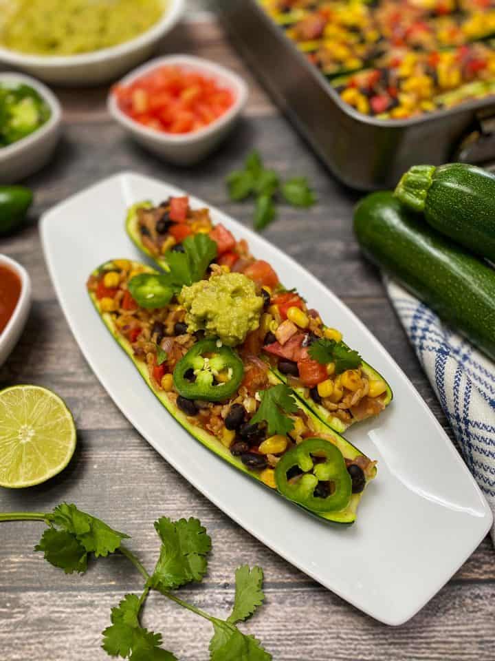 two zucchini halves on white plate stuffed with rice, corn, beans and topped with guacamole
