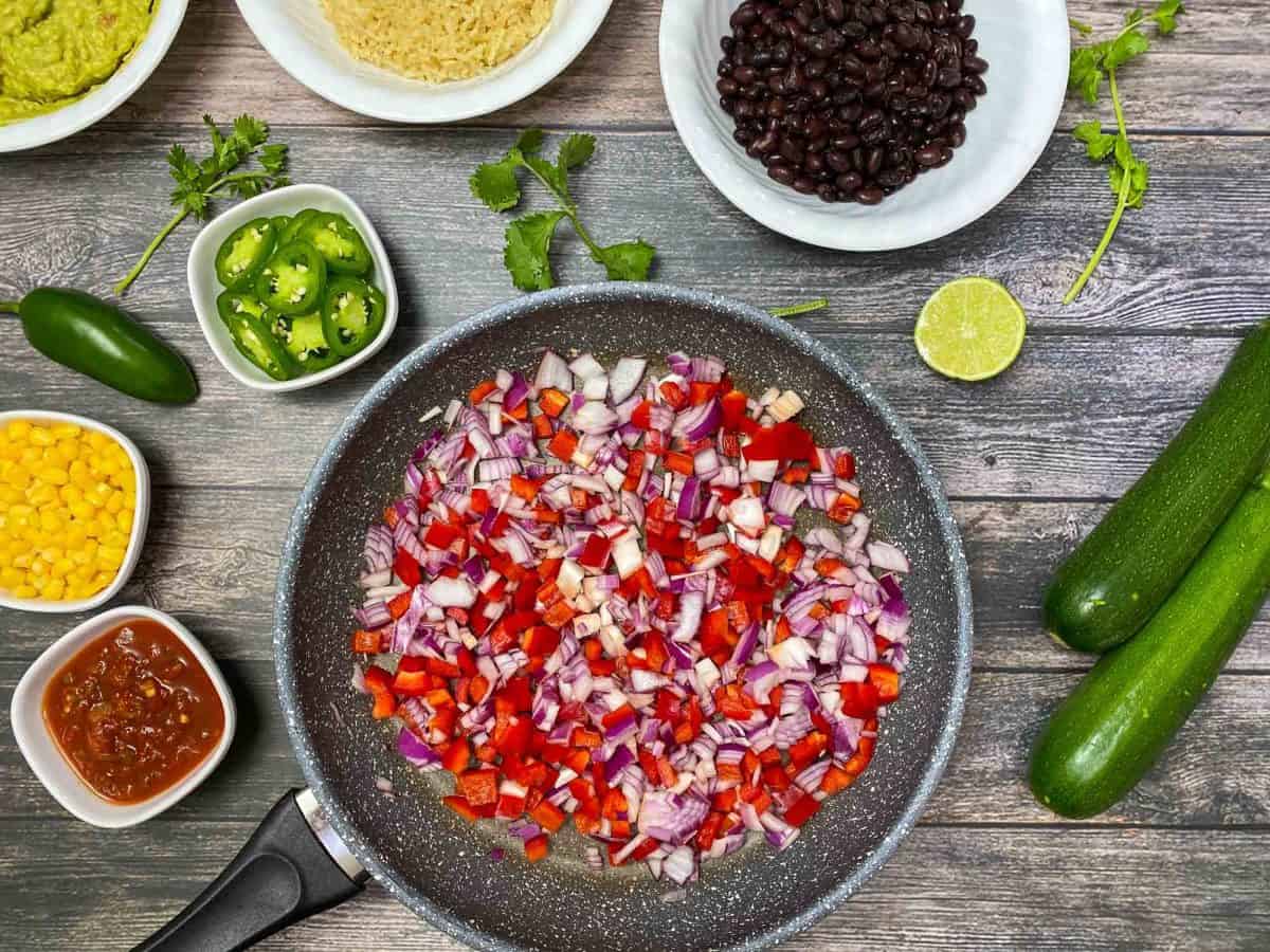 large skillet with diced red onion and pepper on dark grey deck