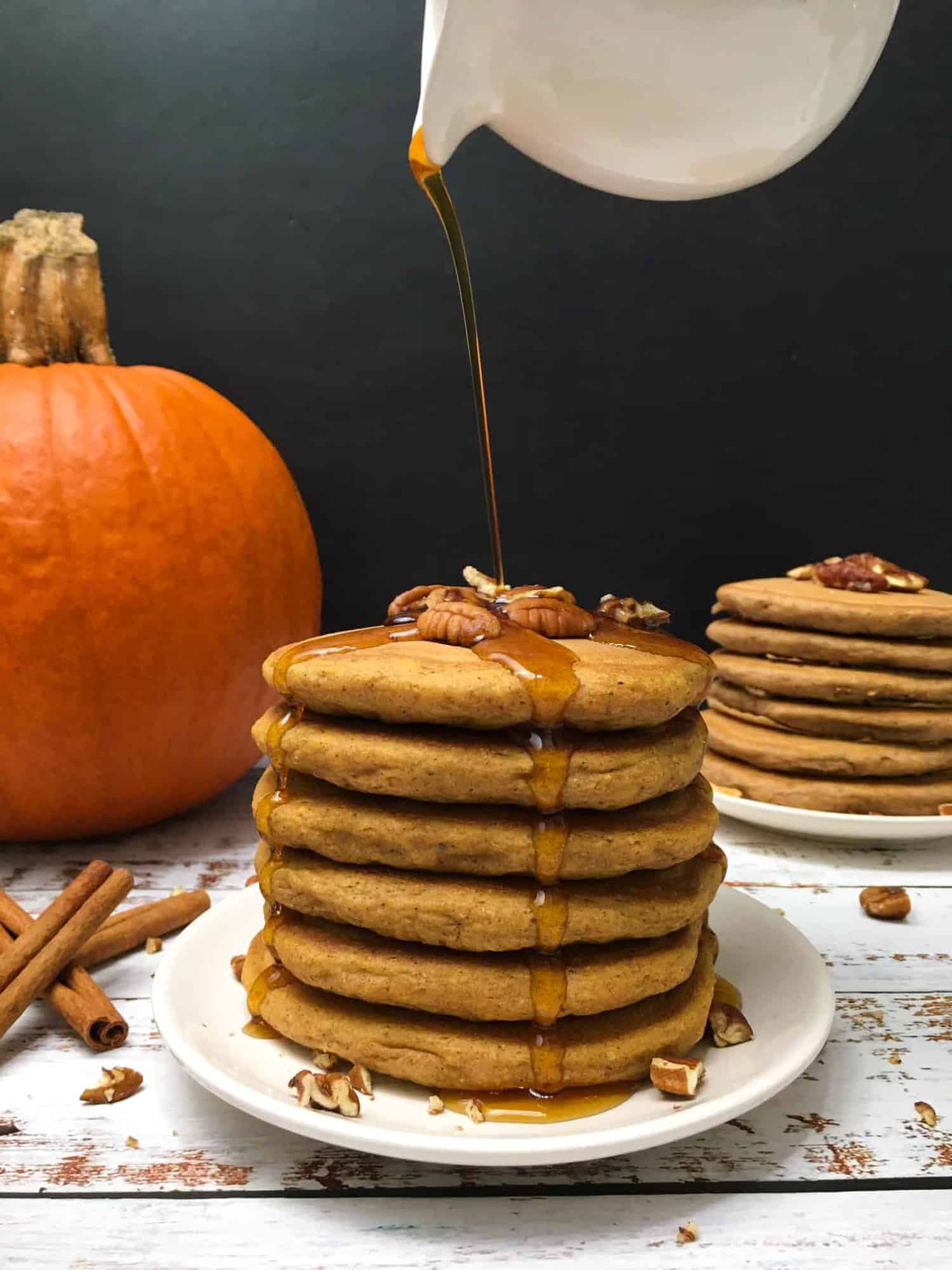 stack of pumpkin spice pancakes in plate with pumpkin in background