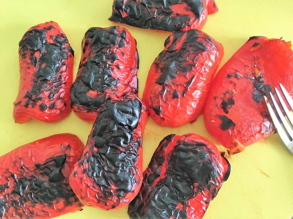 Roasted red peppers with black skin sitting on cutting board.