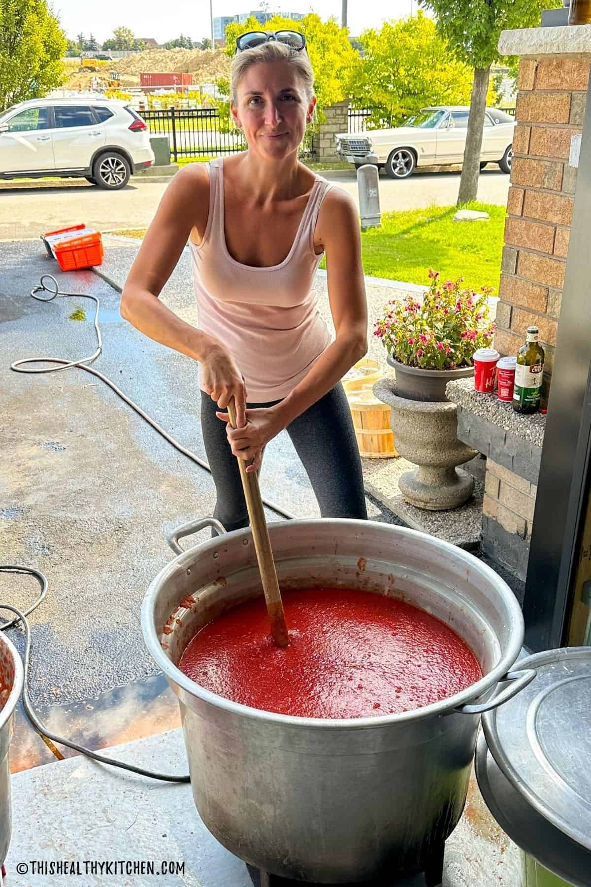 Woman stirring large pot of tomato sauce.