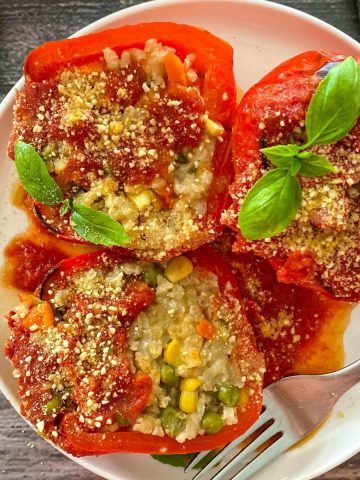 Stuffed pepper sliced in half with risotto inside and whole stuffed pepper beside it on plate.