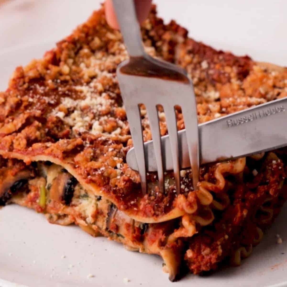 Fork and knife cutting into slice of vegan lasagna.