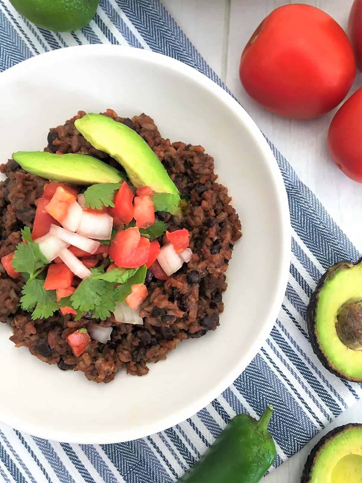 Rice and beans in white dish with chopped tomato, onion, avocado and cilantro on top.