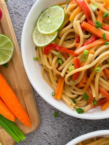 White bowl of noodles, carrots and peppers with lime wedge garnish.