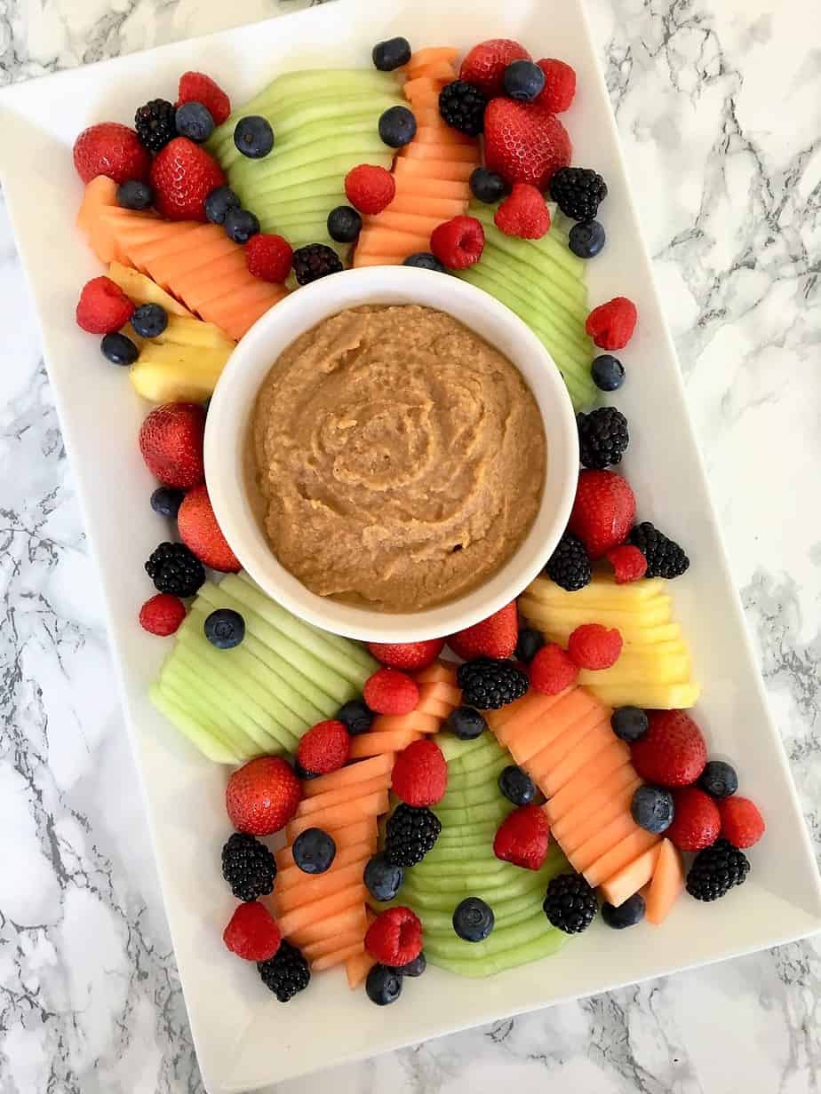 Sweet hummus fruit dip in a bowl on the center of a platter surrounded by fresh fruit
