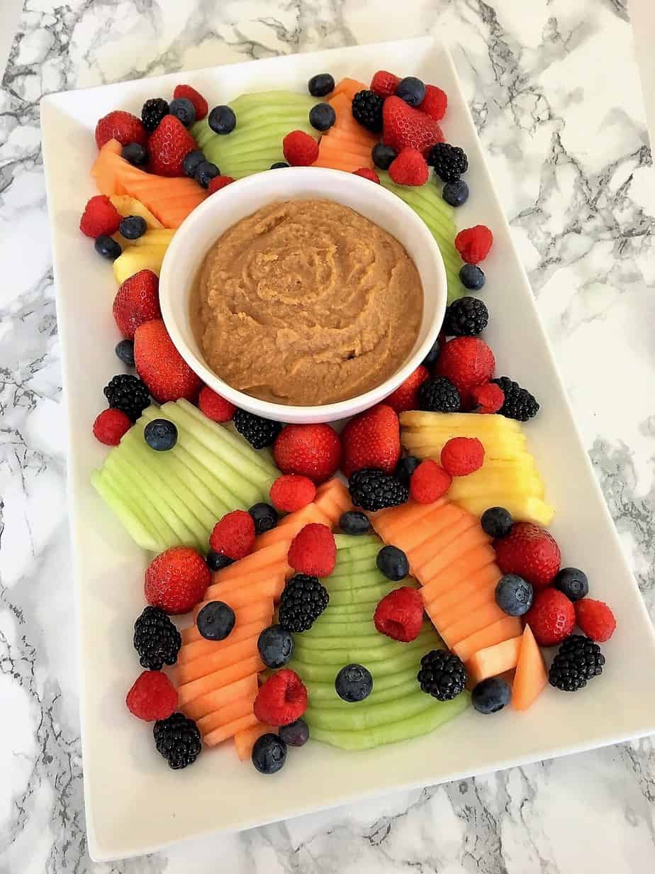 Sweet hummus fruit dip in a bowl on the center of a platter surrounded by fresh fruit