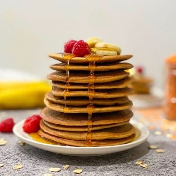 lentil pancakes stacked on plate with fruit on top and syrup dripping down.