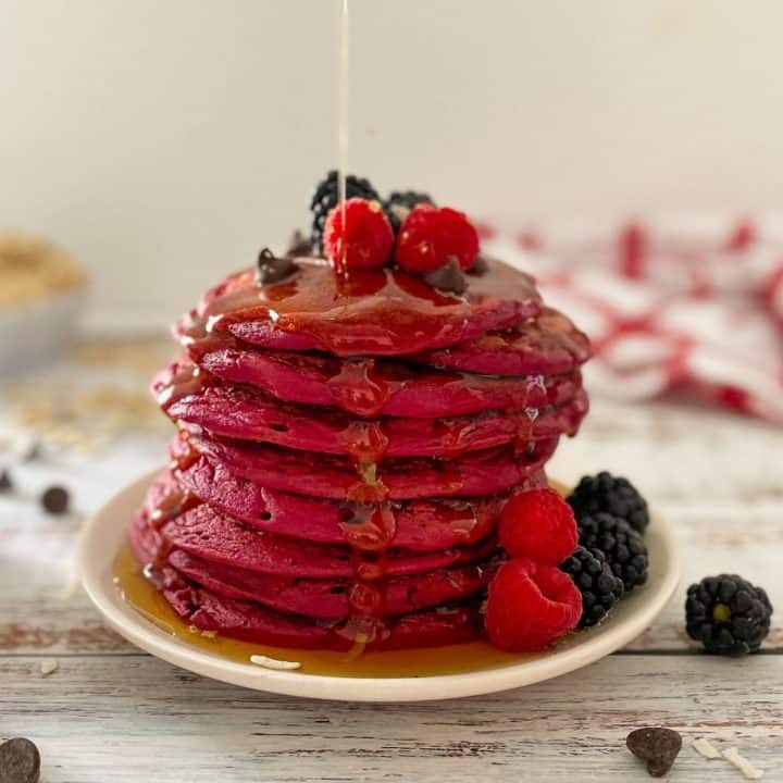 pink pancakes stacked on white plate with syrup dripping down them.
