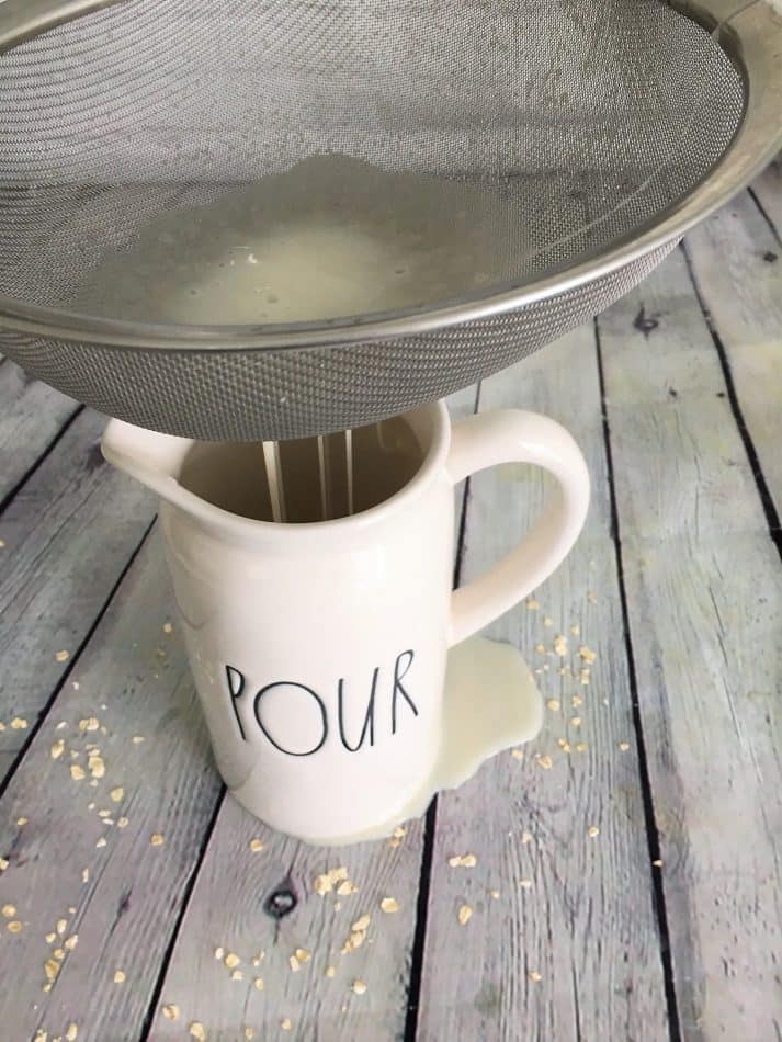 straining oat milk through metal strainer into pitcher