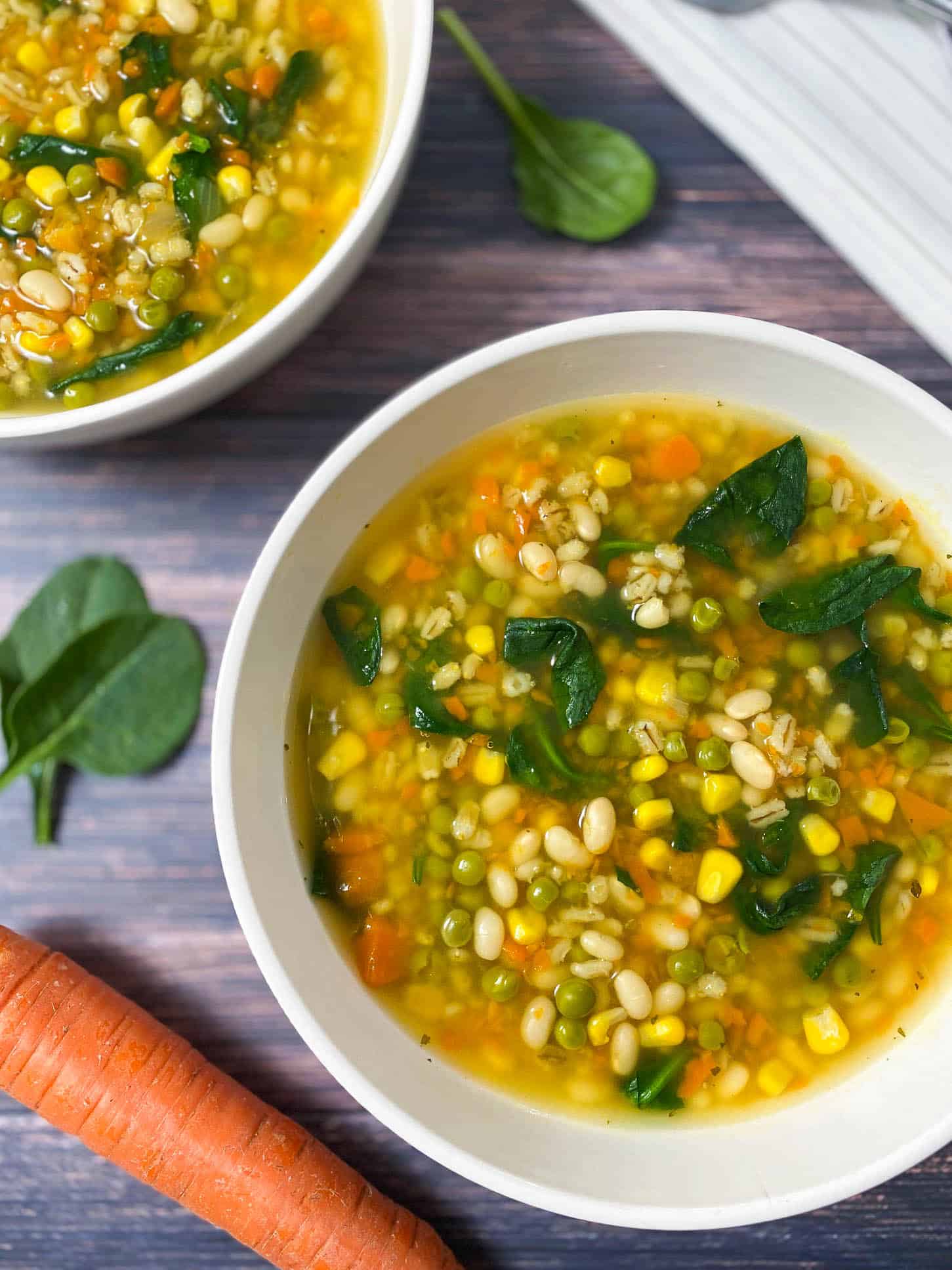 two bowls of vegetable soup with spinach and carrots in background