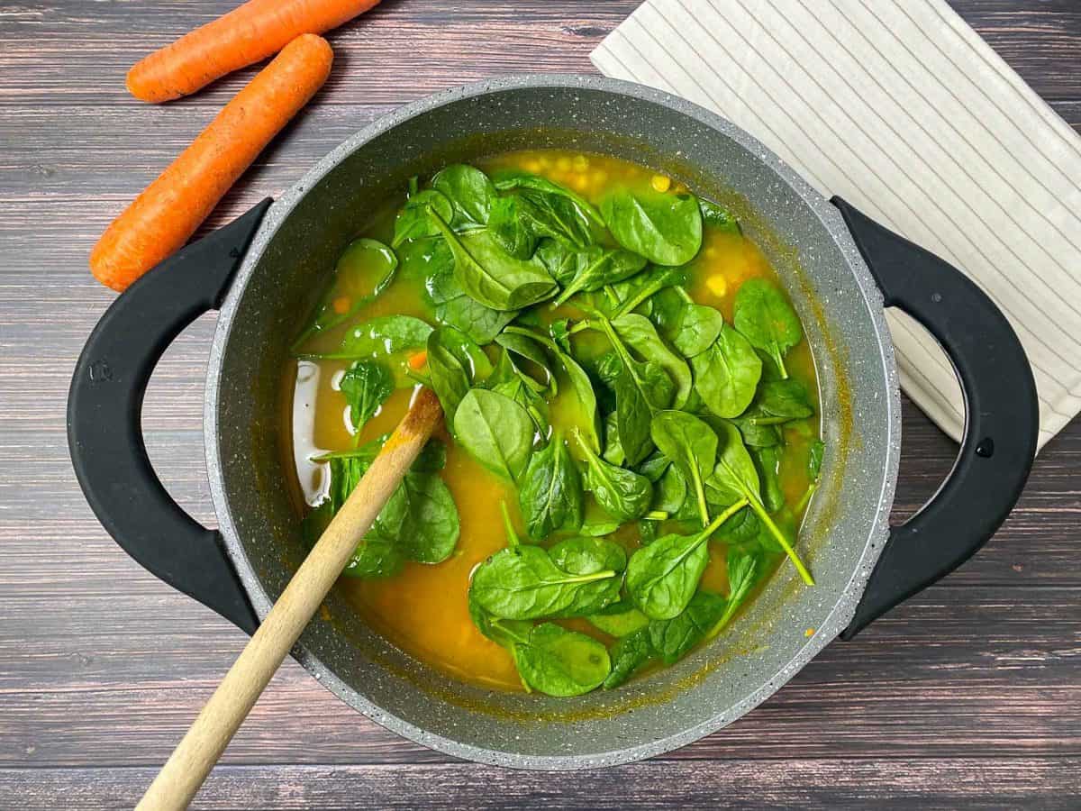 wooden spoon stirring spinach into large pot of soup