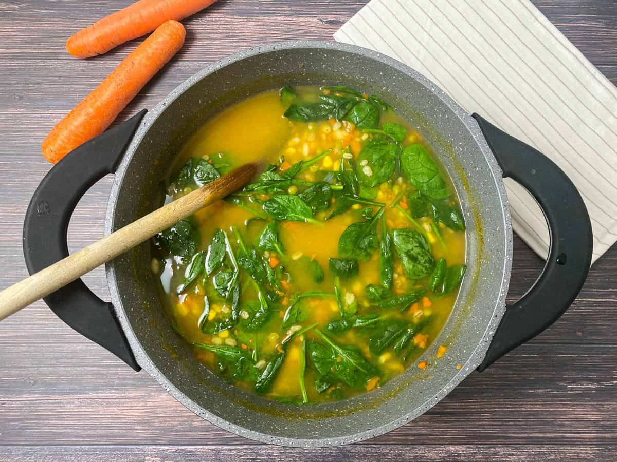 pot of soup with spinach and wooden spoon inside