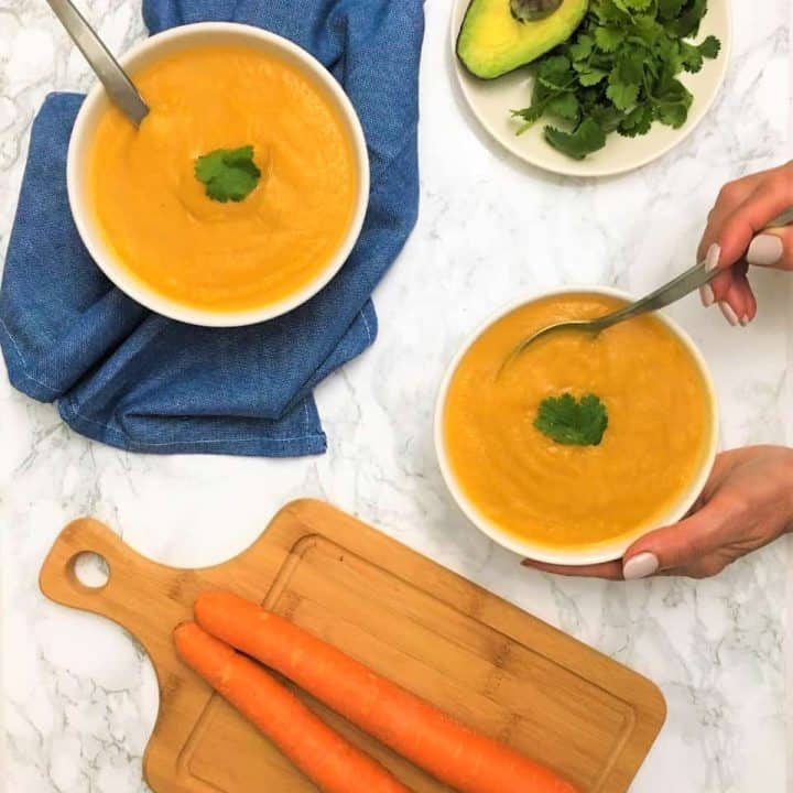 carrot cauliflower soup in bowls with hand holding spoon inside bowl