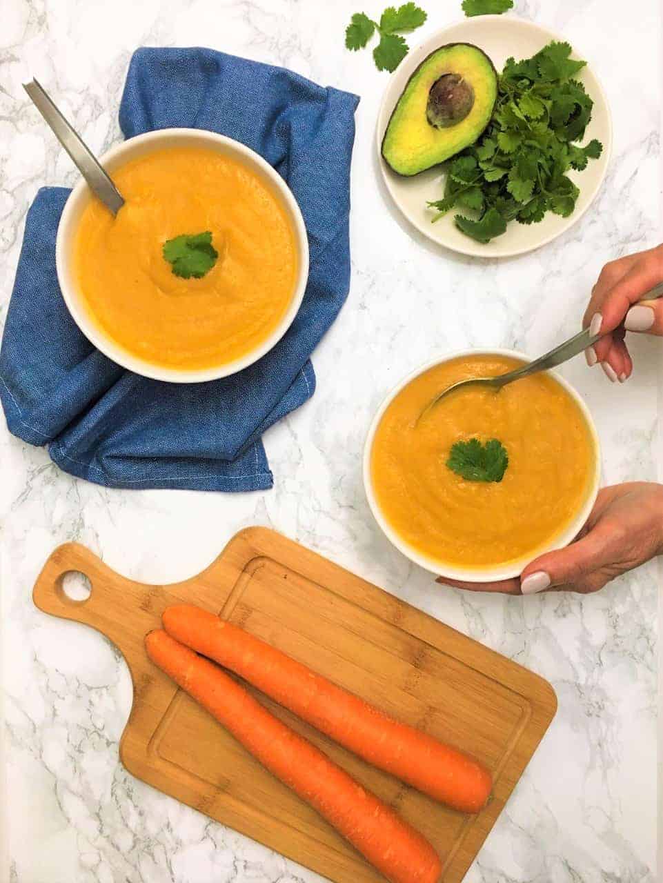 carrot cauliflower soup in bowls with hand holding spoon inside bowl