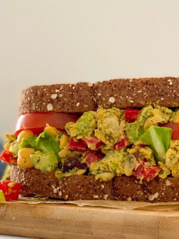 Sandwich resting on cutting board with chickpeas, tomato, celery, peppers and dill.