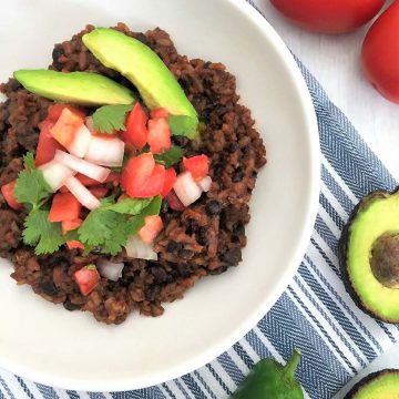 Rice and beans in white plate with tomato, onion and avocado garnish.