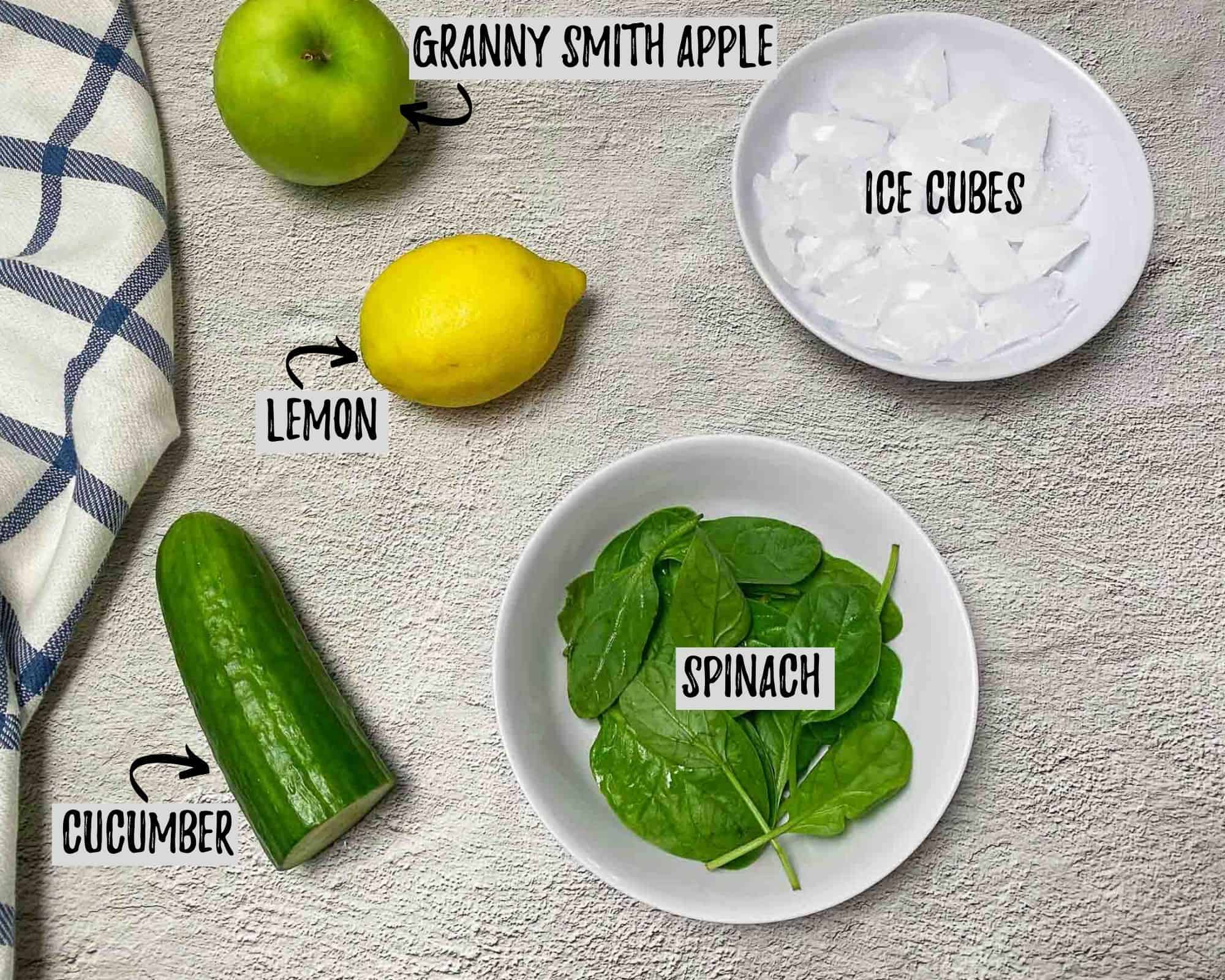 bowl of ice, spinach, lemon, apple and cucumber on concrete surface