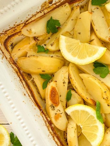 Roasted potatoes in white tray with lemon wedges and parsley garnish.
