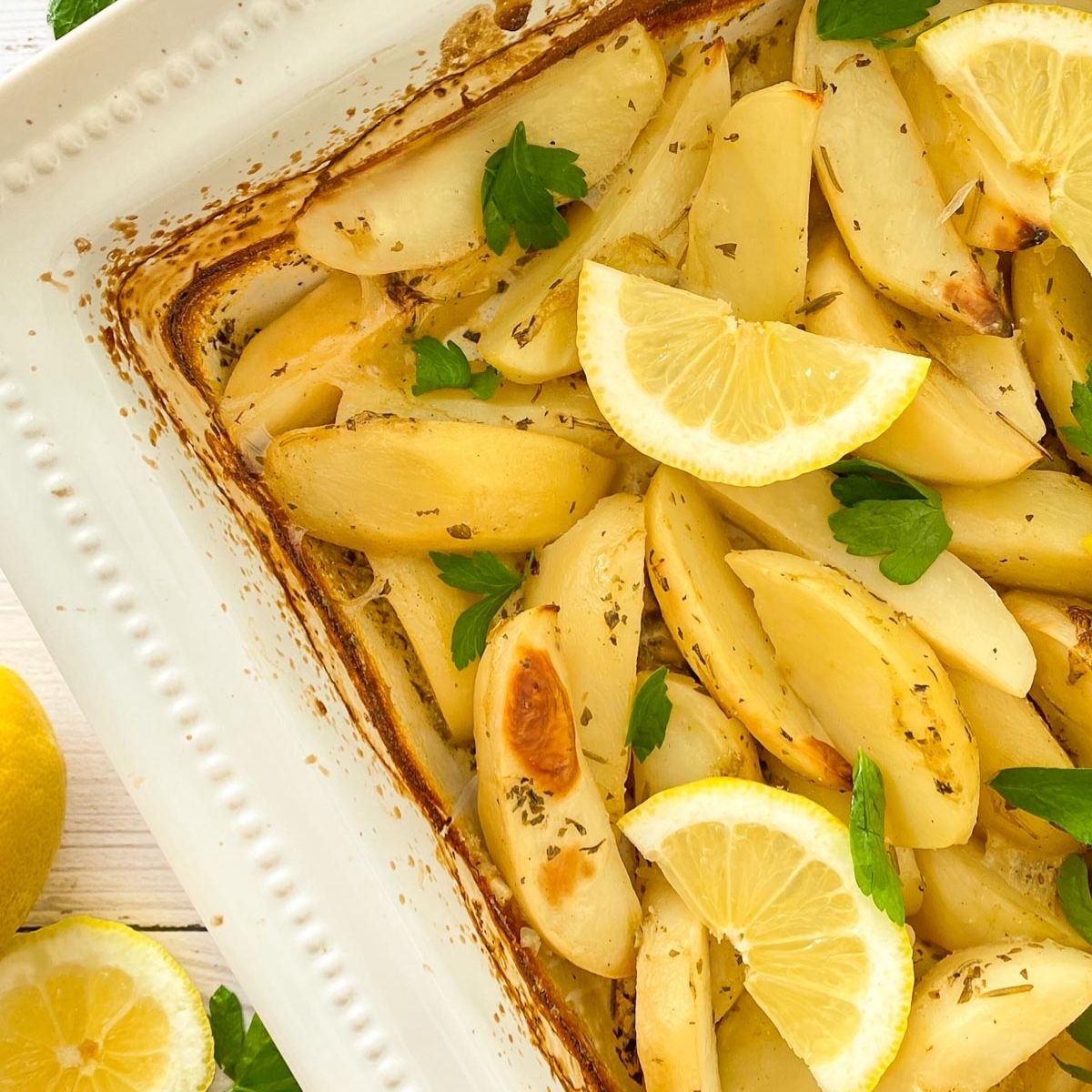 Roasted potatoes in white tray with lemon wedges and parsley garnish.