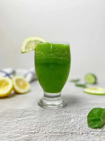 glass of sour apple smoothie with lemon wedge garnish
