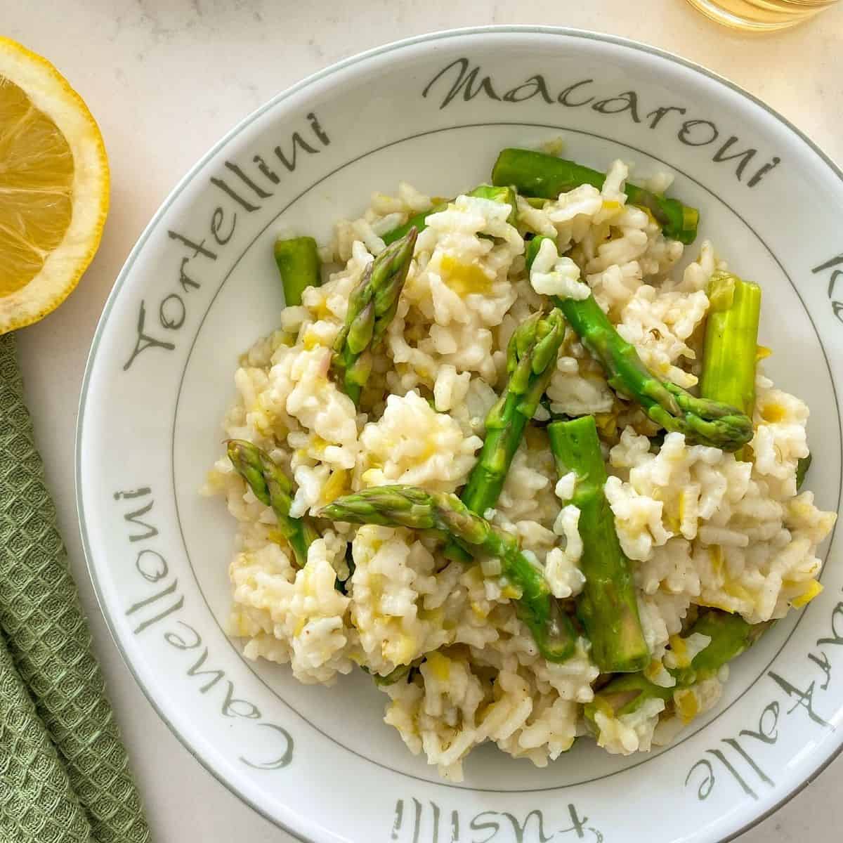 Risotto with asparagus in round bowl with lemon on the side.