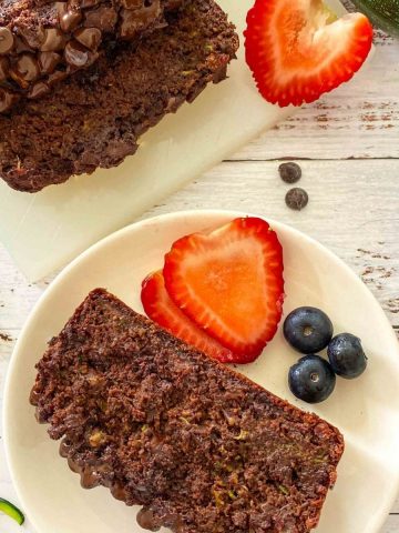 Slice of chocolate zucchini bread on white plate with strawberries and blueberries beside it.