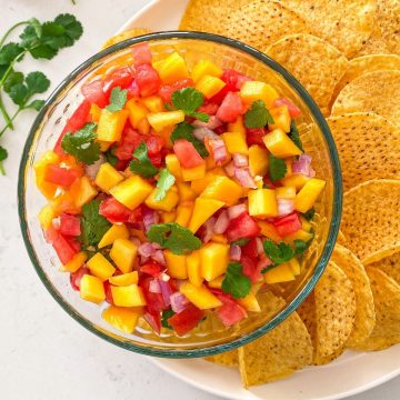 Glass bowl with mango habanero salsa inside on plate of chips.