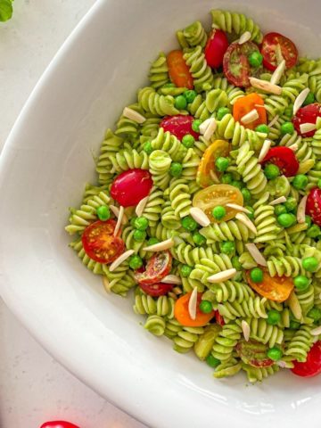 Large serving bowl with pesto pasta salad inside with cherry tomatoes and slivered almonds on top.